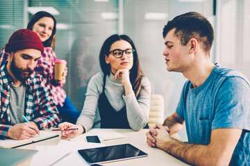 Group of casual dressed students sitting at meeting table and discussing ideas for common project having brainstorming meeting.Team of male and female designers collaborating on development startup