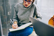 © BullRun - Copped view of pensive young woman in eyeglasses writing down essay in notebook doing homework.Smart concentrated hipster student making notes in notepad preparing for upcoming exams