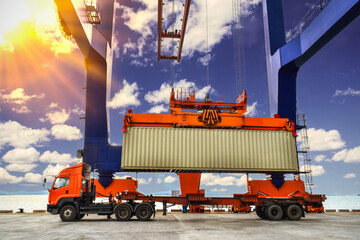 Wall Mural - Quay crane lifting up 40 feets container from trailer using spreader at container port with blue sky background and backlight. Container loading unloading activities at seaport.