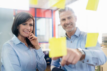 Smiling Businesswoman And Businessman Looking At Adhesive Notes In A Factory Office