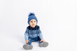 © Any Grant - Baby 8 months old boy sitting on a white isolated background in warm winter clothes and a hat, children's fashion, advertising children's clothing, space for text