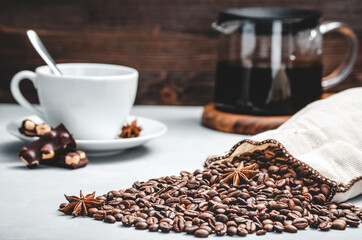 Wall Mural - roasted coffee beans are scattered from a bag on a stone light background with a Cup and a glass coffee pot, selective focus with a small depth of field coffee beans