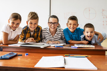 Wall Mural - Portrait of primary school kids with they female teacher.They sitting at the desk in classroom.