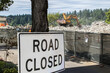 Road closed sign adjacent to a construction site where a large track mounted backhoe is demolishing a building.