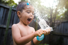 3 Year Old Mixed Race Boy Plays Excitedly With Water Bombs In Suburban Backyard