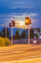 A Full Moon Rising Between Traffic Lights At An Intersection