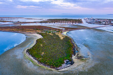 Aerial View Of A Small Island In Front Of A Boat Marina With Bird Life Around Its Edges