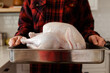 © Goodness Grace Photography/Stocksy - Anonymous man wearing flannel shirt holds a raw, uncooked turkey in pan for Thanksgiving dinner