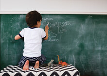 Boy Traces Dinosaurs On Chalkboard