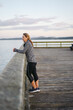 © Rob and Julia Campbell/Stocksy - Woman leaning on pier railing at sunset.