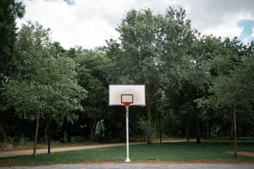 basketball court in a park with trees with white board and no net on the hoop