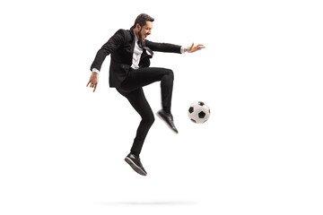 Wall Mural - Full length profile shot of a man in a black suit kicking a soccer ball