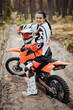 © Fxquadro - Happy brunette girl wearing motorcycle outfit sitting on her bike off-road in the woods
