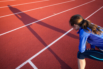 Pretty female runner stretching before her run at a track and field stadium