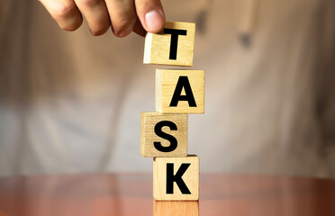 Businesswoman hand holding wooden cube block with TASK business word on table background. List and Schedule concept