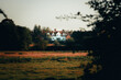 © Aidan - White country house in the distance over a field during sunset