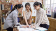 © PRPicturesProduction - Working as a team. young modern female people in smart casual wear planning business strategy while pointing at document paper together in office. three lady coworkers discussing on chart graph.