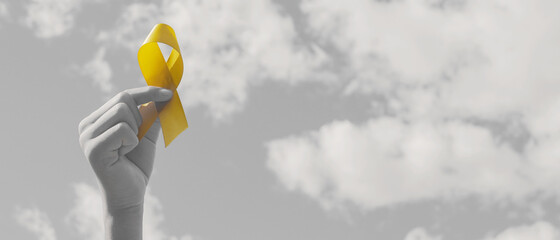 Wall Mural - Hands holding yellow gold ribbon over  sky, Sarcoma Awareness, Bone cancer, childhood cancer awareness, September yellow, World Suicide Prevention Day concept