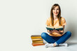 © Alex - Young woman holds a book while sitting on the floor on a light background. Education concept, exam preparation. Banner
