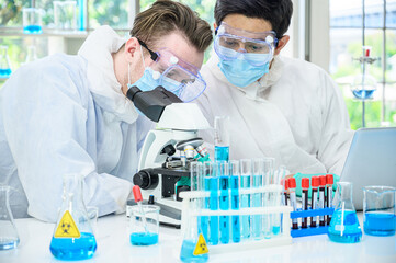 Couple male scientist wearing protection suit working with Microscope and many lab equipment for research Coronavirus  vaccine at laboratory.