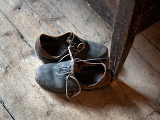 Pair of old worn out leather retro shoes on a vintage wooden floor by the table.  Historical peasant footwear