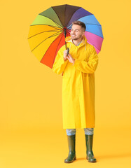 Young man in raincoat and with umbrella on color background