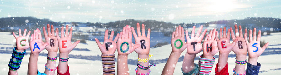 Children Hands Building Colorful English Word Care For Others. Snowy Winter Background With Snowflakes