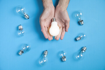 Wall Mural - Male hands holding light bulb in the blue background.