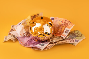 Golden piggy bank with cash money, euro and dollar banknotes. Golden money box, huge savings, money accumulation. Money pig, money saving, moneybox, finance and investments, budget concept. Copyspace.