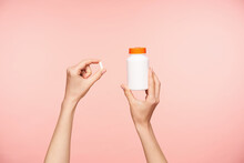 Cropped Photo Of Raised Female's Well-groomed Hands Holding White Pill And Bottle With Orange Cover, Taking Vitamins While Posing Over Pink Background