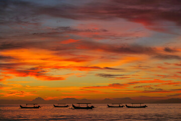 Wall Mural - Fishermen boats silhouettes in tropical fiery sunset light. View from Kuta beach, Bali island, Indonesia 