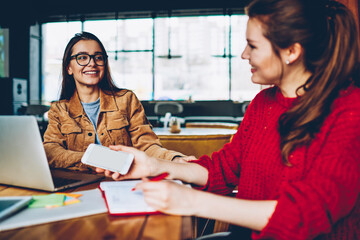 Wall Mural - selective focus on smiling hipster girl in eyewear looking to her female friend sitting near and enj