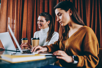 Wall Mural - smiling hipster girl watching funny videos while female friend near waiting important webinar on lap