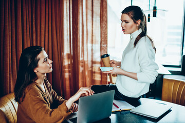 Wall Mural - millennial female freelancers discussing ideas for teamwork during coffee break at cafeteria, young 