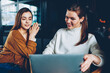 © BullRun - Cheerful hipster girls making video call using web camera on netbook device connected to wifi indoors, positive women spending free time together using laptop for watching comedy movie online