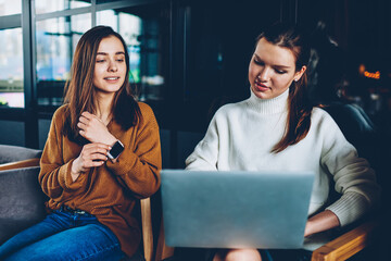 Wall Mural - positive female student watching funny video with friend using laptop device connected to cafeteria 