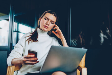 Wall Mural - Serious female student checking time and notification on modern smartphone device sitting with laptop indoors, millennial woman using technologies for learning and studying at coworking space
