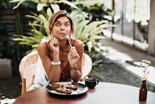 Tanned Happy Girl In Brown Bra Looks Surprised, Holds Fork And Makes Funny Face. Woman Sits In Cafe And Eats Waffle With Chocolate Sauce