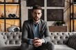© opolja - Cool and handsome. Good looking young man in full suit sitting on the sofa while spending time indoors.