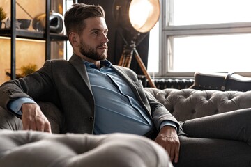 Wall Mural - Cool and handsome. Good looking young man in full suit sitting on the sofa while spending time indoors.