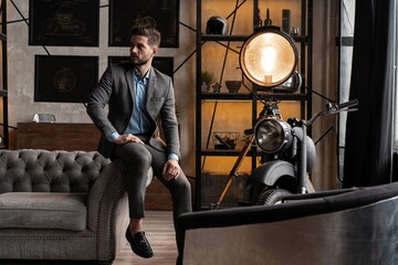 Wall Mural - Cool and handsome. Good looking young man in full suit sitting on the sofa while spending time indoors.