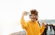 © Alessandro Biascioli - Young Afro man taking self video while listening music with wireless headphones - Happy mixed race guy having fun with new technology apps for mobile smartphone - Millennial lifestyle concept
