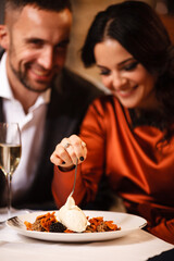 Wall Mural - Romance and dating concept. Young couple man and woman celebrating and eating delicious dessert in restaurant. Two people male and female in elegant evening suit and dress on romantic dinner