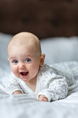 A cute little baby is smiling lying on the bed on a white sheet in the parents bedroom. Closeup portrait of newborn baby looking at camera