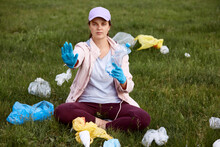 Activist Picking Up Trash In Field, Sitting On Green Grass And Holding Plastic Bottle, Showing Stop Sign With Her Palm, Female Calls For Saving Our Planet From Pollution,solving Ecological Problems.