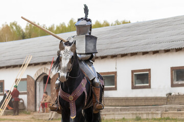 A knight in vintage armor of the 15th century rides a horse across a field for a tournament