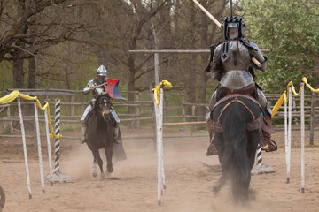 A knight in vintage armor of the 15th century rides a horse across a field for a tournament