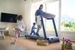 © trevor adeline/Caia Image - Kids running around their mother exercising on treadmill in living room