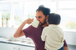 © trevor adeline/Caia Image - Man drinking coffee and holding son in morning kitchen