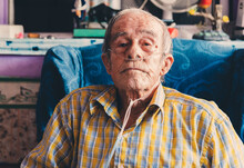 Portrait Of An Old Man Sitting At Home With Oxygen In His Nose.